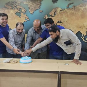 Sky Limit staff cutting the 18-year celebration cake with IndiGo Airlines team in front of a world map background.
